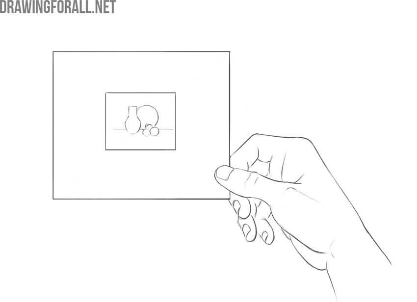 Hand holding a paper viewfinder to frame a still life composition with a vase and fruit.